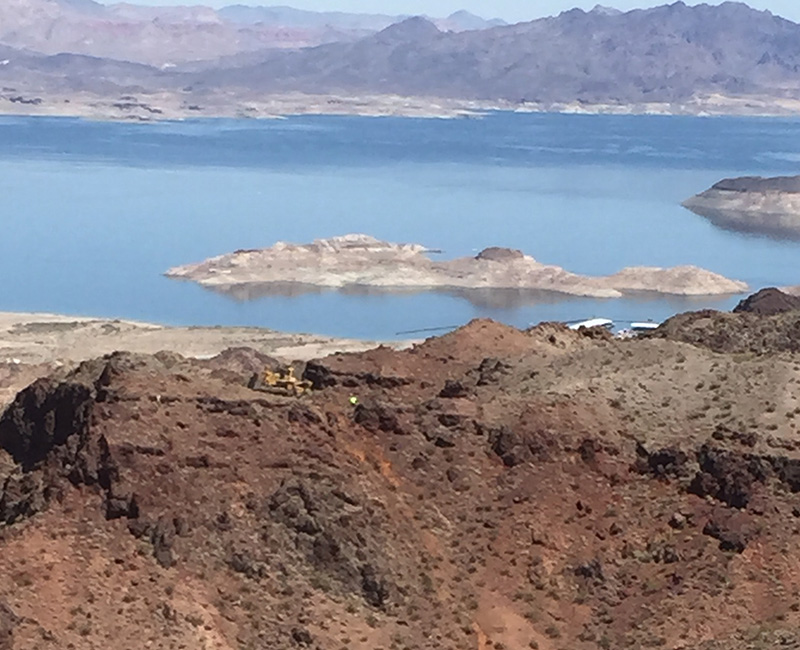 Lake Mead in the background with construction equipment and a worker on the hill in front of the lake