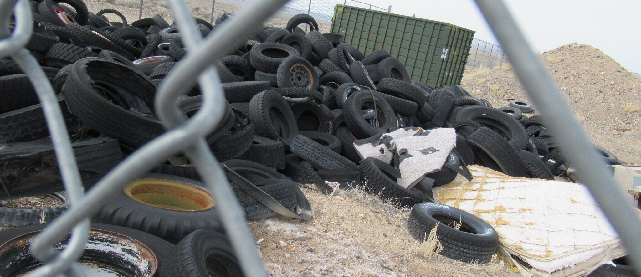 Tires and a large shipping container sit in a fenced landfill