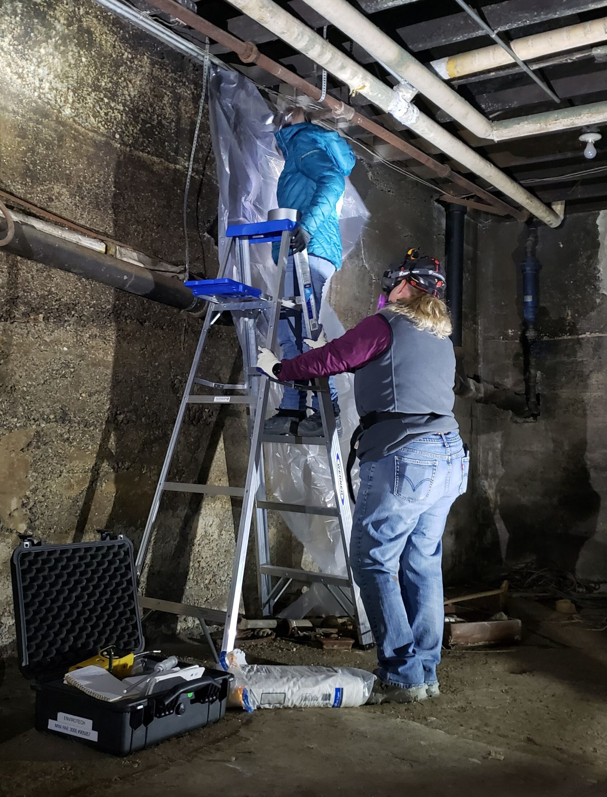 BEC Environmental Scientists use plastic sheeting to cover ventalated areas in a basement in preparation for radon testing.